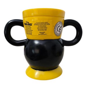 May include: A yellow and black Disney On Ice mug with two black handles. The mug has a rounded base and a cylindrical top. The mug has text on the side, including the Disney On Ice logo and other information.