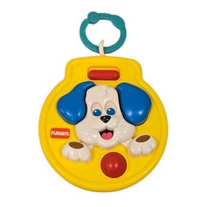 May include: A yellow Playskool toy featuring a white puppy face with blue ears, a red button, and a teal ring for hanging. The puppy has a smiling expression with a pink tongue. The toy is designed for babies and toddlers.