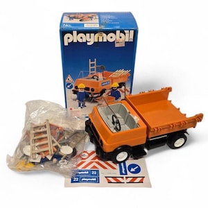 May include: A Playmobil construction truck toy set in orange and black, with a box. The truck has a tipping bed and a cab with a steering wheel. The box shows an illustration of the truck and figures. Extra accessories are in a plastic bag.