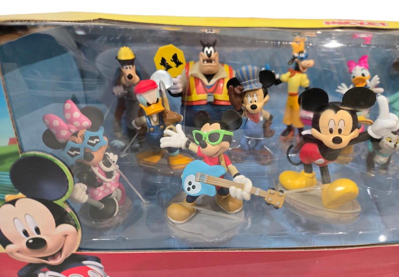 May include: A collection of Disney character figurines, including Mickey Mouse, Minnie Mouse, Donald Duck, Goofy, and others. The figures are in various poses and outfits, with vibrant colors and detailed designs. The set is packaged in a clear plastic container.