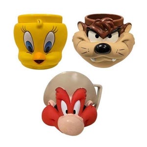 Puede incluir: Tres tazas de cerámica con personajes de Looney Tunes. Las tazas tienen la forma de Piolín, Taz y Yosemite Sam. La taza de Piolín es amarilla, la taza de Taz es marrón y marrón, y la taza de Yosemite Sam es marrón y roja.