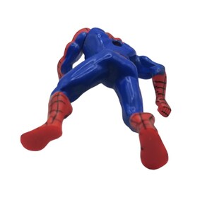 May include: A blue and red Spider-Man action figure, viewed from the back. The figure is in a dynamic pose, with its arms and legs extended. The costume is primarily blue with red accents on the gloves, boots, and mask.