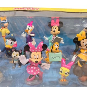 May include: A collection of Disney character figurines, including Mickey Mouse, Minnie Mouse, Donald Duck, and Pluto. The figurines are in various poses and outfits, with vibrant colors and detailed designs. The set is displayed in a clear plastic case.