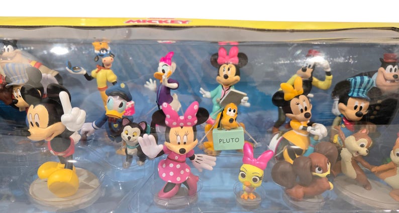 May include: A collection of Disney character figurines, including Mickey Mouse, Minnie Mouse, Donald Duck, and Pluto. The figurines are in various poses and outfits, with vibrant colors and detailed designs. The set is displayed in a clear plastic case.
