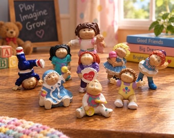 May include: A collection of eight small Cabbage Patch Kids figurines in various poses and outfits. One figure stands on its hands, another holds a heart sign that says I Love You, and others hold items like an ice cream cone or a rattle.
