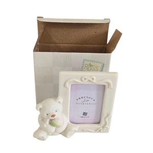 Puede incluir: Marco de fotos de cerámica color crema con diseño de lazo y figura de osito de peluche. El marco lleva la inscripción "PRECIOUS keepsakes" y mide 5 cm x 7,6 cm. El marco está junto a una caja de cartón abierta.