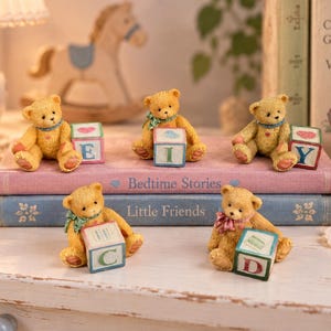 May include: Five small, golden-brown teddy bear figurines are arranged on two stacked books titled Bedtime Stories and Little Friends. Each bear sits beside a colourful wooden alphabet block featuring the letters E, I, Y, C, and D.