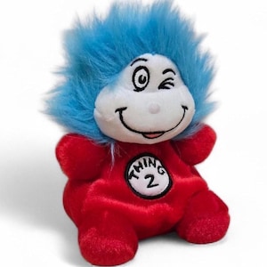 May include: A plush toy of Thing 2 from the Dr. Seuss book, "The Cat in the Hat." The toy has a red body, blue fuzzy hair, and a white face with a winking eye and a smiling mouth. The number "2" is on the chest.