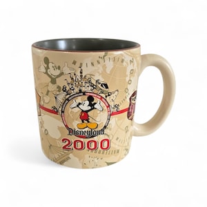 Pode incluir: Caneca de cer&acirc;mica bege com Mickey Mouse e o logotipo da Disneyland 2000. A caneca tem uma al&ccedil;a creme e um interior cinza escuro. O design inclui um mapa-m&uacute;ndi e v&aacute;rios &iacute;cones da Disneyland.
