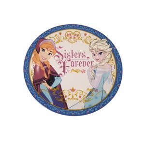 Op de afbeelding: Ronde plaat met Anna en Elsa uit Frozen, met de tekst "Sisters Forever". De plaat heeft een blauwe rand met bloemen- en stippatronen. Anna draagt een paarse cape en Elsa een blauwe jurk.