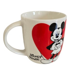Op de afbeelding: Witte keramische mok met een gebogen handvat, met Mickey Mouse voor een groot rood hart. De woorden "Mickey Mouse" staan op de zijkant gedrukt. Een klassiek Disney-ontwerp.