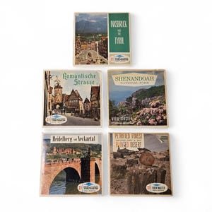 May include: A selection of vintage View-Master reels displaying scenic locations. The reels feature images of Innsbruck, Tyrol, Romantische Strasse, Shenandoah National Park, Heidelberg, and Petrified Forest. Each reel is small and rectangular with a colourful image.