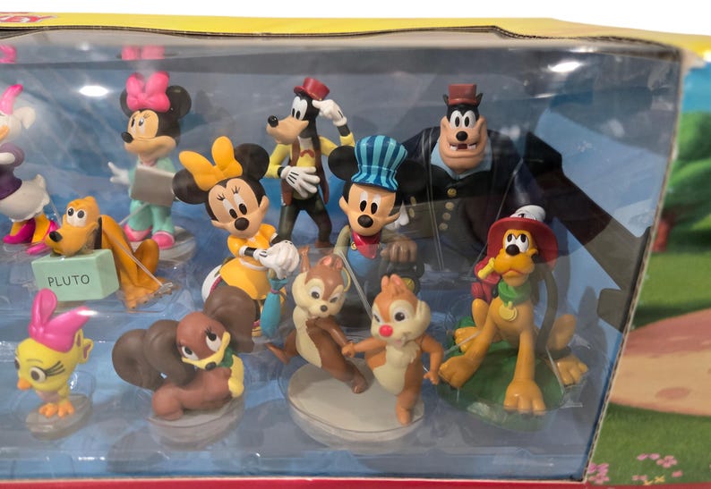 May include: A collection of Disney character figurines, including Mickey Mouse, Minnie Mouse, Goofy, Pluto, and Chip and Dale. The figures are in a clear plastic display case, with vibrant colors and detailed designs. The Pluto figure has a sign that says "PLUTO".