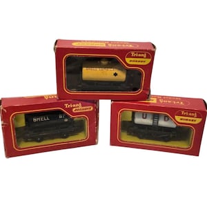 Puede incluir: Tres vagones de tren modelo Tri-ang Hornby vintage en sus cajas rojas originales. Cada caja tiene una ventana transparente que muestra el vagón de tren en miniatura en el interior. Los vagones están etiquetados "SHELL", "BP" y "UUD".