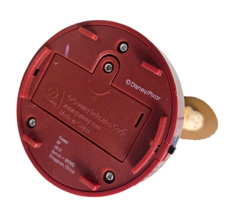 May include: A red plastic base of a Woody figurine, with the text "&copy;Disney/Pixar" and "Gemmy Industries Corp." The base has a battery compartment and several screws. The figurine is made in China.