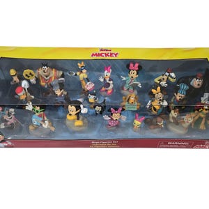 May include: A boxed set of Disney figurines featuring Mickey Mouse and friends. The set includes various characters in colorful outfits, displayed on individual bases. The packaging is a yellow and clear plastic box with the words "Junior Mickey" on the top.