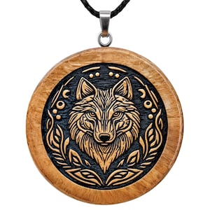 May include: A circular wooden pendant featuring a carved wolf head at the centre, set against a dark, textured background. The wolf is framed by stylised leaf patterns and small circular motifs. The pendant hangs from a black cord with a silver bail.