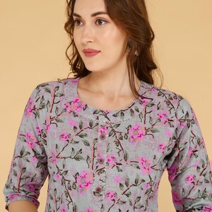 May include: A grey top with a floral pattern in pink and green. The top has a round neckline, three-quarter sleeves, and a button-down front. The floral design is spread across the fabric.