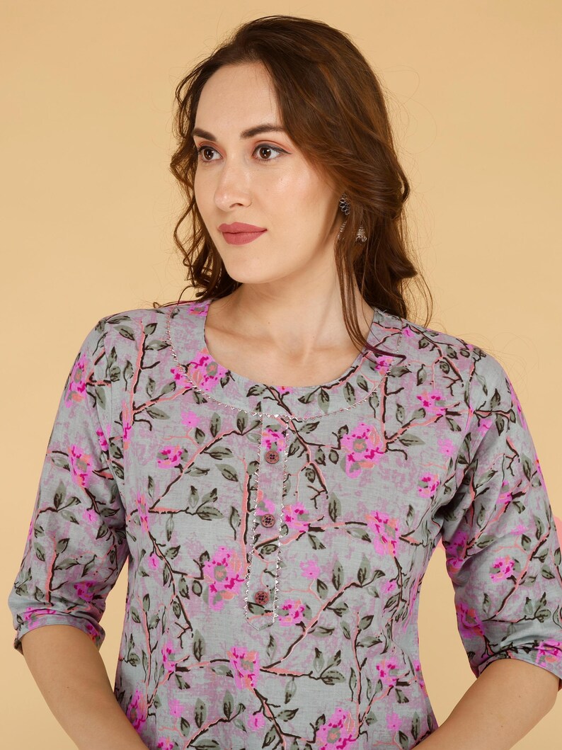 May include: A grey top with a floral pattern in pink and green. The top has a round neckline, three-quarter sleeves, and a button-down front. The floral design is spread across the fabric.
