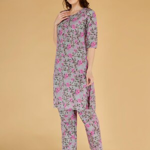 May include: A two-piece pajama set with a grey floral print. The set includes a top and matching trousers. The floral pattern is pink. The model is wearing pink sandals.