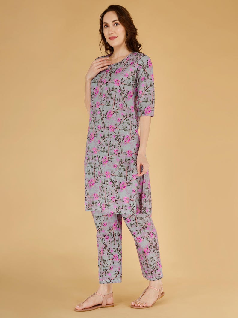 May include: A two-piece pajama set with a grey floral print. The set includes a top and matching trousers. The floral pattern is pink. The model is wearing pink sandals.