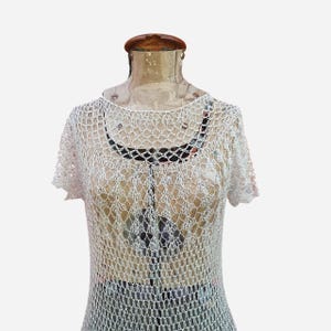 K&ouml;nnte beinhalten: Ein wei&szlig;es, kurz&auml;rmeliges H&auml;keltop mit rundem Ausschnitt. Das offene Design des Tops l&auml;sst einen Blick auf die darunterliegende Unterw&auml;sche zu. Das Top wird auf einer Vintage-Mannequin pr&auml;sentiert.