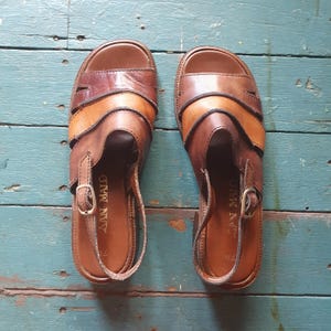 Peut inclure: Une paire de sandales en cuir marron avec une fermeture à bride et boucle. Les sandales présentent un design superposé avec des nuances de marron et de beige. La marque "SAN MALO" est visible sur la semelle intérieure. Pointure 37.