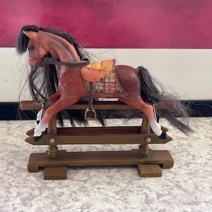 May include: A wooden rocking horse figurine with a brown body, black mane and tail, and a tan saddle. The horse has white accents on its legs and is mounted on a wooden base. The figurine is a decorative item.