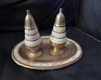 May include: Two gold salt and pepper shakers with a white and gold checkered pattern on a gold tray with a white and gold checkered pattern.