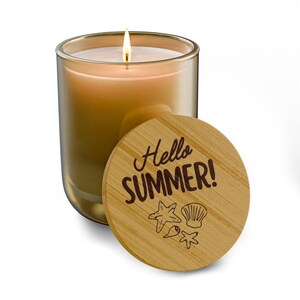 Pode incluir: Uma vela acesa num frasco de vidro transparente com tampa de madeira. A tampa é gravada com as palavras "Hello SUMMER!" e ilustrações de estrelas do mar, conchas e peixes. A vela tem um tom dourado quente.