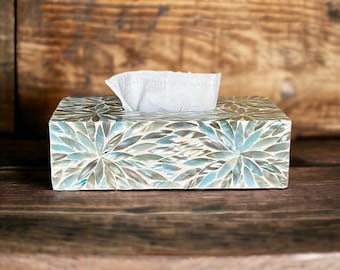 May include: A rectangular tissue box cover featuring an iridescent mosaic pattern of mother-of-pearl shell pieces in shades of blue, green, and grey. The surface is covered in a floral-like arrangement of petals, with a white tissue protruding.