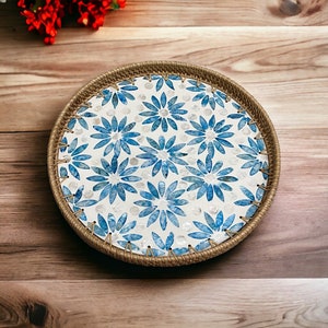 Könnte beinhalten: Runder Weidenkorb mit floralem Muster. Der Korb hat einen weißen Hintergrund mit blauen Blumenmustern und einen gewebten Rand. Die Blumen haben einen Aquarelleffekt. Der Korb hat einen Durchmesser von etwa 30 cm.