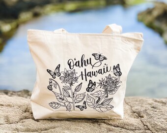 Puede incluir: Una bolsa de lona blanca con texto negro e ilustraciones. El texto dice "Oahu Hawaii" y presenta un diseño floral con mariposas.