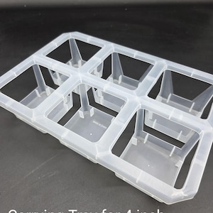 May include: A clear plastic carrying tray designed to hold six 4-inch pots. The tray has a rectangular shape with individual square compartments and a sturdy frame. The text "Carrying Tray for 4 inch pots - Clear" is visible.