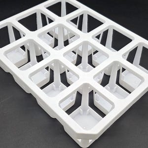 May include: A white plastic carrying tray for 3-inch square pots. The tray has a grid-like design with square openings and supporting structures. The text "Carrying Tray for 3 Inch Square Pot (White)" is visible.