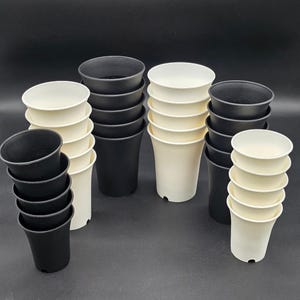 May include: A collection of small, black and off-white plastic plant pots. The pots are stacked in groups, showcasing their simple, rounded design. The background is a solid black, highlighting the pots' shapes and colors.