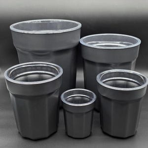 May include: A set of five matte black cylindrical containers of varying sizes, each featuring a smooth, clear plastic rim at the top opening. The containers have a slightly tapered shape with vertical ridges along the exterior walls.