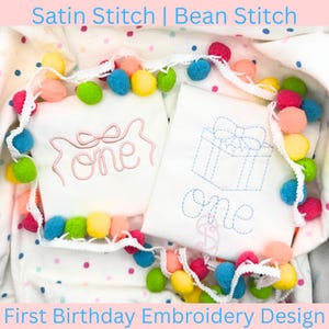 May include: Two white onesies with embroidered designs for a first birthday. One has a pink bow and the word "one", the other has a gift box and the word "one". A colorful pom-pom garland surrounds the onesies. Text at the top says "Satin Stitch | Bean Stitch".