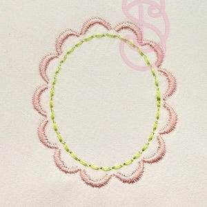 May include: Embroidered design featuring a scalloped pink border and a green inner circle. A light pink decorative element is in the upper right corner. The design is on a cream-colored fabric, suitable for embroidery projects or textile art.