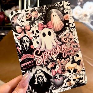 May include: A rectangular sticker sheet featuring a collage of black, white, and pink illustrations including ghosts, skulls, bows, and the text "Spooky", "it's SPOOKY season", "Creep it Cute", and "BABE" with various spooky-themed icons.