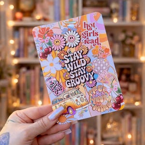 May include: A colorful sticker with a retro design featuring daisies, a VW bus, cherries, and the text "Stay Wild Stay Groovy" and "Hot Girls Read". The sticker has a light pink, orange, and yellow color scheme.