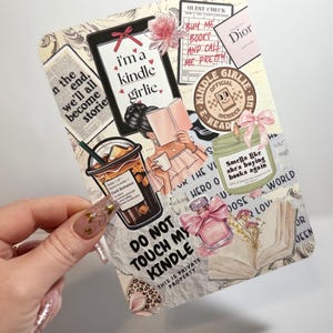 May include: A rectangular sticker featuring a collage of book-themed illustrations including a person reading, a coffee cup, a candle labeled 'Smells like she's buying books again', a perfume bottle, and text reading 'i'm a kindle girlie' and 'DO NOT TOUCH MY KINDLE'.