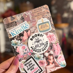 May include: A Kindle case covered in stickers with a floral and book theme. Stickers include the words "Kindle," "Books!", and "When I die delete my kindle history." Other stickers feature a rose in a glass dome, a butterfly, and a girl reading.