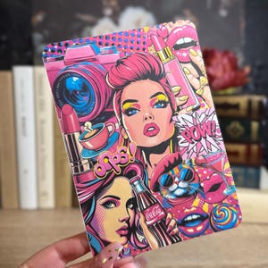 May include: A pop art style print featuring a woman with pink hair, a camera, lipstick, and the word "Oops!". The design incorporates vibrant pink, blue, and yellow colors, with a comic book aesthetic. A Coca-Cola bottle is also visible.