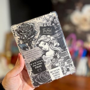 May include: Clear phone case with a black and white collage design. The design includes roses, a portrait of a woman, and text that reads "The End", "CAUTION may contain smut", and "DON'T TALK TO ME MY FAVORITE CHARACTER JUST DIED".