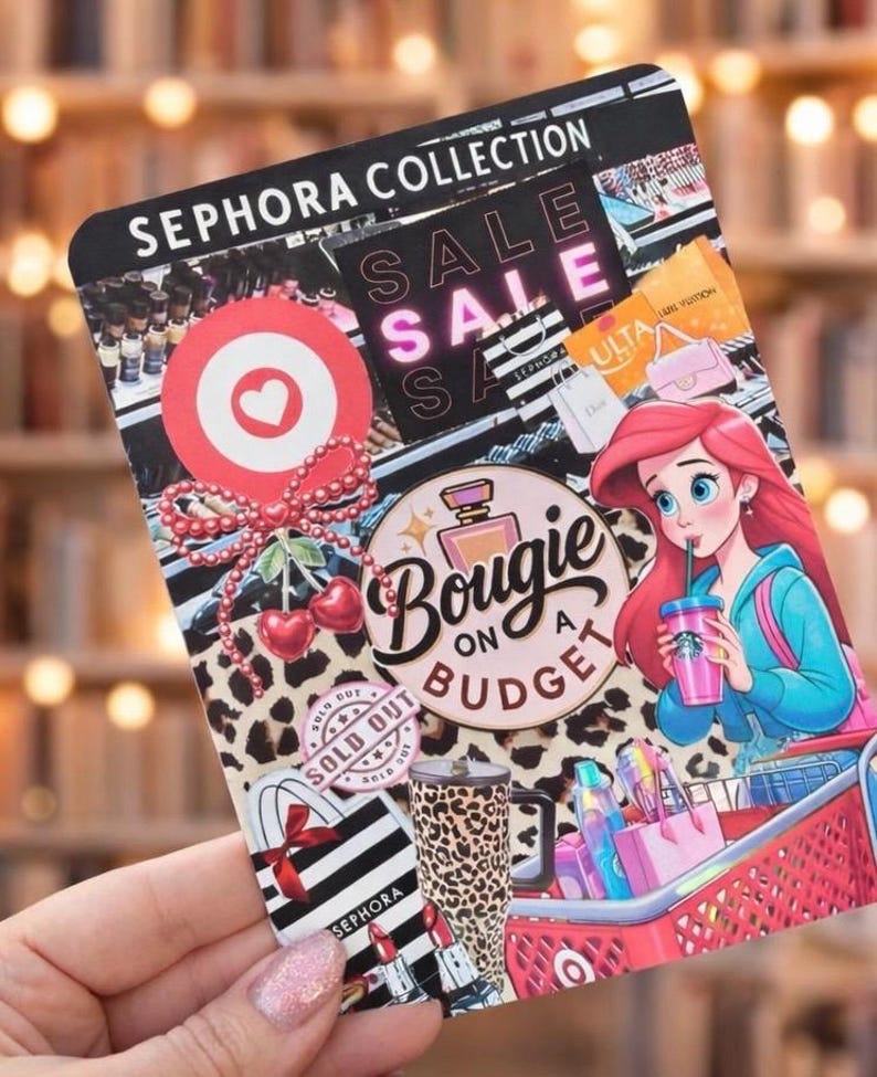 May include: A decorative card with the text "SEPHORA COLLECTION" and "SALE" in pink. The card features a cartoon of a mermaid drinking from a cup, a shopping cart, and various beauty product illustrations.