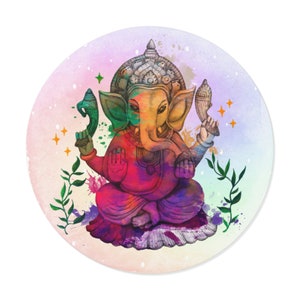 Op de afbeelding: Rond decoratief item met een aquarel illustratie van Ganesha, de hindoeïstische godheid. Het kunstwerk toont Ganesha zittend, in levendige tinten geel, rood, paars en groen. De achtergrond heeft een zachte pastelkleurige gradiënt met kleurensplashes en steraccenten.