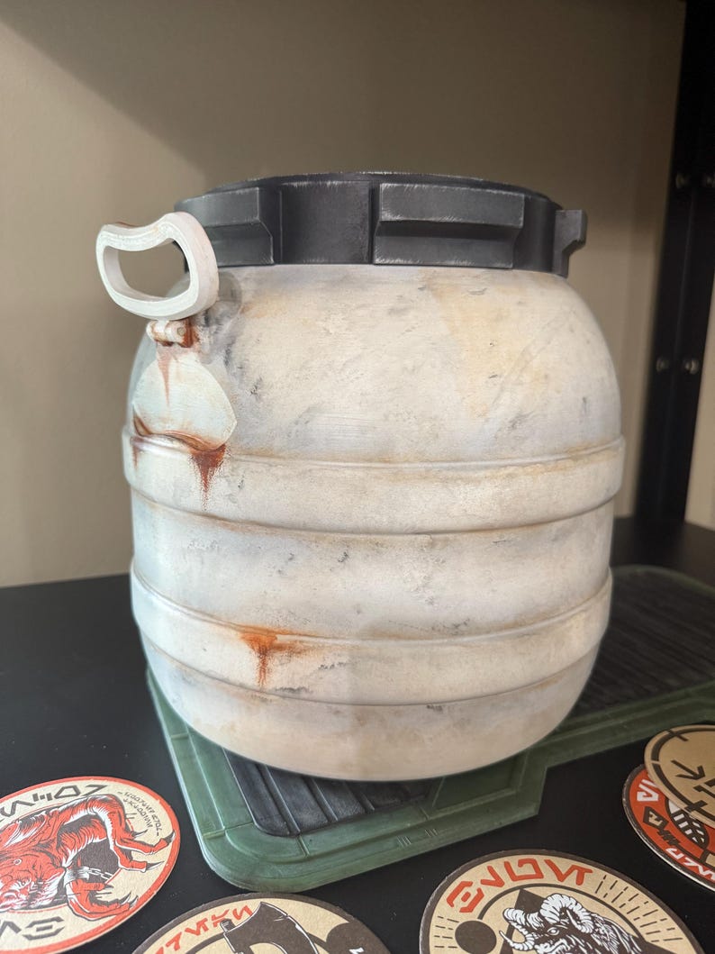 May include: A weathered, cylindrical container with a black top and a white handle. The body is off-white with horizontal bands and rust-colored streaks. The container sits on a green, textured surface, with several circular stickers visible.
