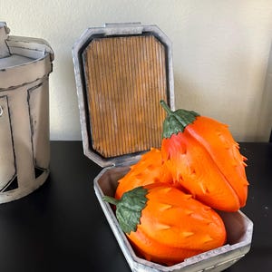 Könnte beinhalten: Drei orangefarbene Früchte mit Stacheln und grünen Blättern in einer weißen Box mit einem Holzdeckel. Die Box ist geöffnet und die Früchte sind im Inneren sichtbar.