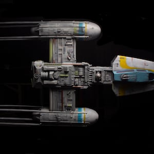 May include: A model of a gray and white spaceship with yellow and blue accents. The spaceship has two wings and a long, narrow body.